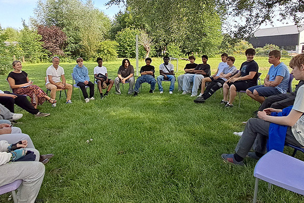 Leerlingen en leerkrachten in een cirkel op stoelen in een tuin