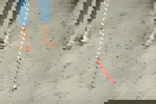 Close up van iemand die sandalen aan heeft en wandelt met een blindenstok.