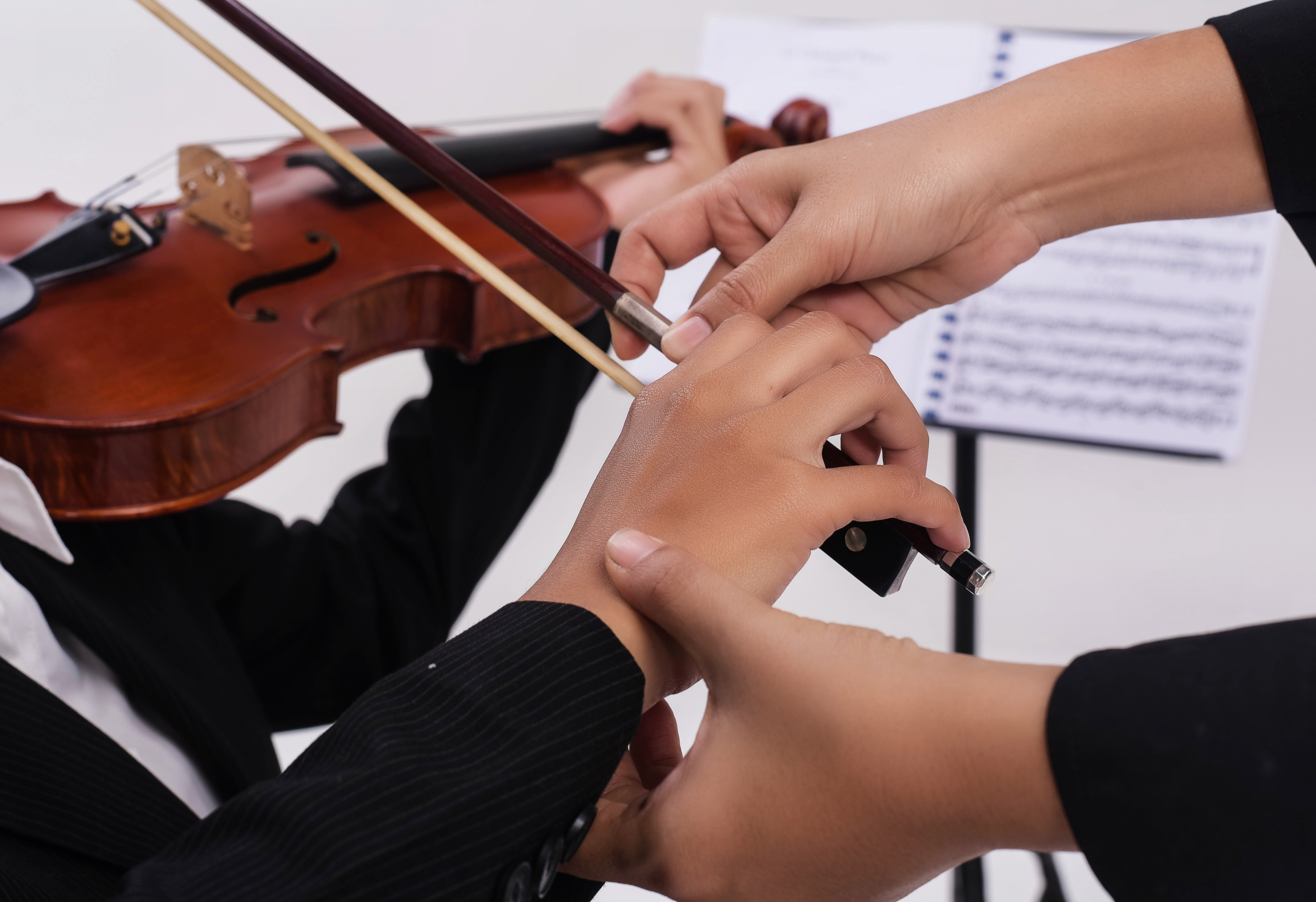 Close up van handen kind dat viool speelt en handen leerkracht die het kind helpen bij de juiste positie op het instrument