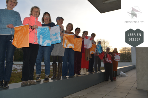 Rij van vrouwen op een laag muurtje buiten, ze houden turnzakjes vast. Logo van het CVO in rechterbovenhoek