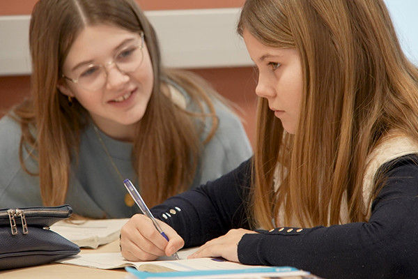twee tienermeisjes aan een schoolbank vullen samen cursus in