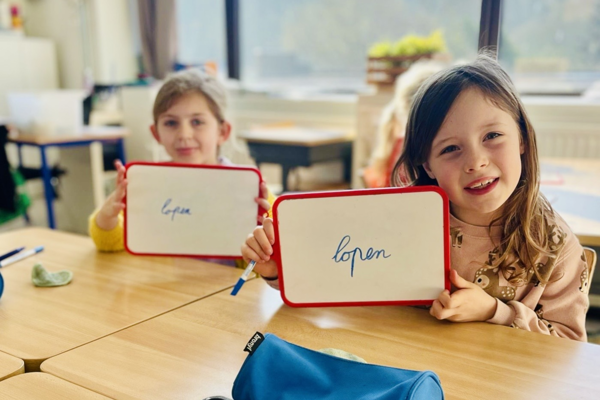 Twee Meisjes Tonen Op Bordjes Hoe Je 'Lopen' Schrijft Rh