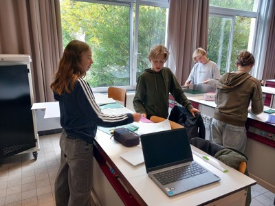 4 leerlingen staan in een klaslokaal rond een projecttafel