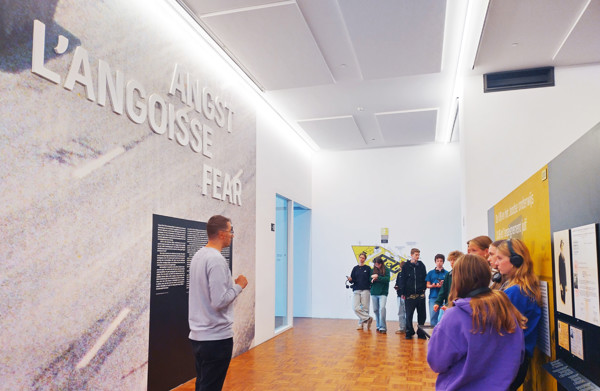 Leraar staat met leerlingen in een hal van een tentoonstelling en geeft uitleg