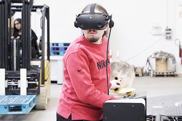 leerling met VR-bril aan toestel en rijdende heftruck in de achtergrond