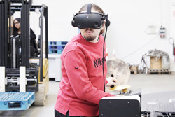 leerling met VR-bril aan toestel en rijdende heftruck in de achtergrond