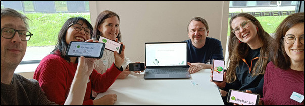 6 mannen en vrouwen rond een tafel die hun smartphonescherm tonen in een selfie
