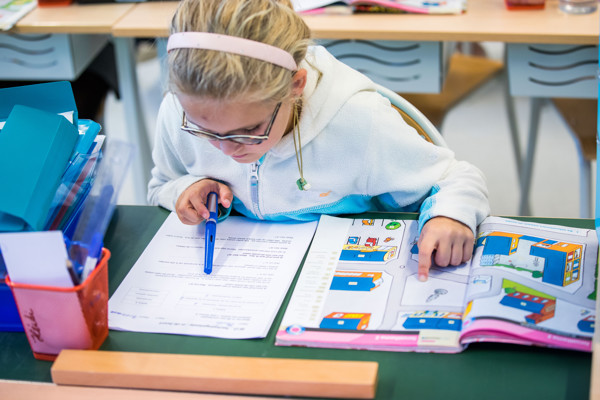 Meisje zit aan een bureau in de klas en zoekt oplossingen in een boek.